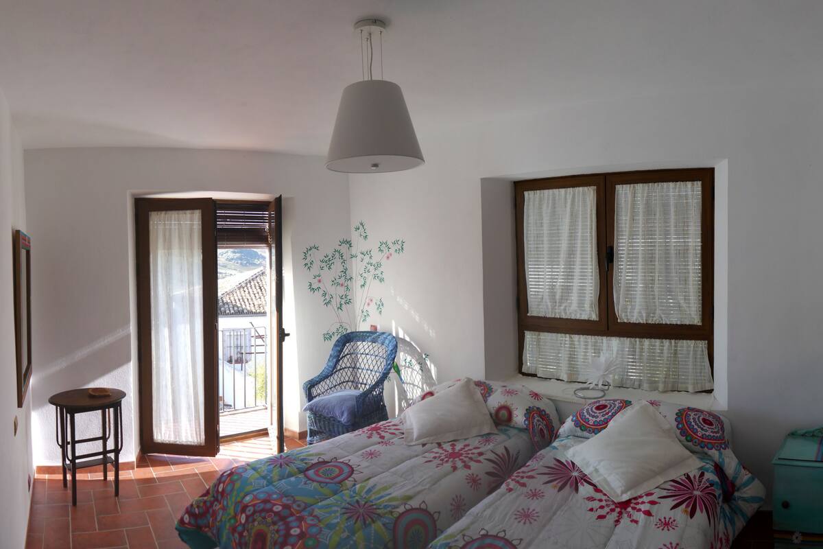 A bedroom with a bed, a chair, a window, and a hanging light fixture.