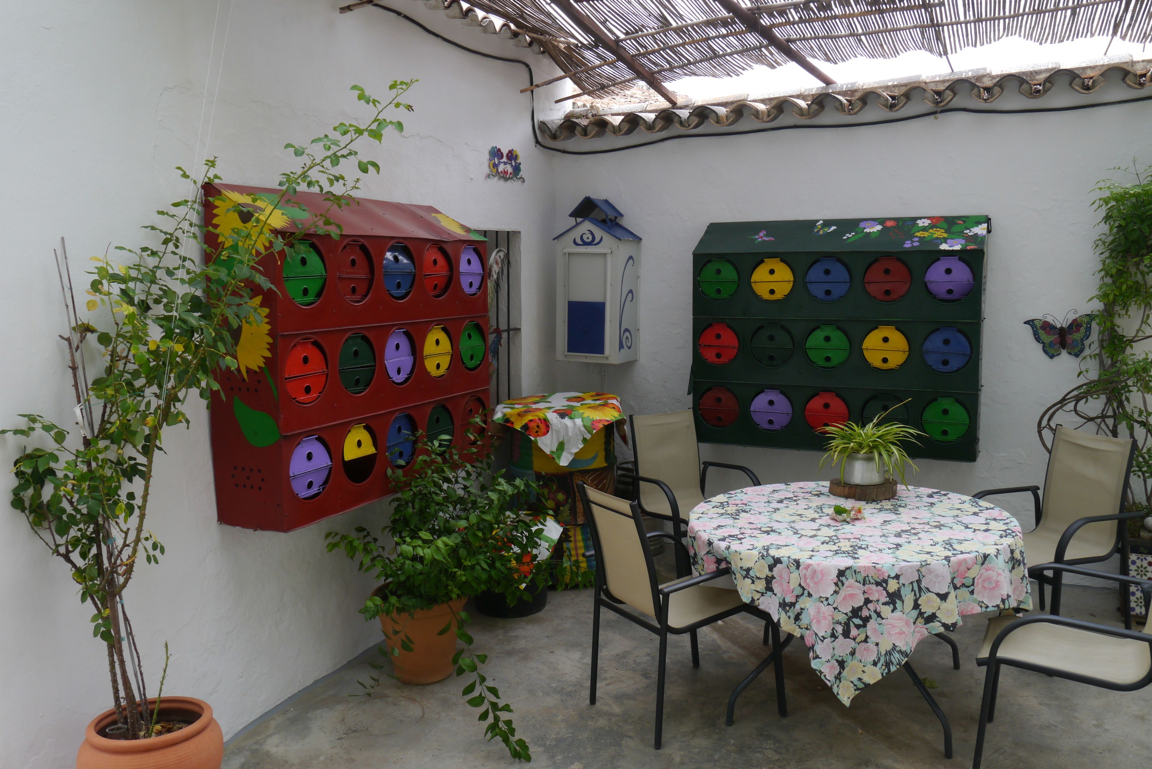 A patio with a round table, chairs, potted plants, and colorful wall decorations.