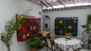 A patio with a round table, chairs, potted plants, and colorful wall decorations.