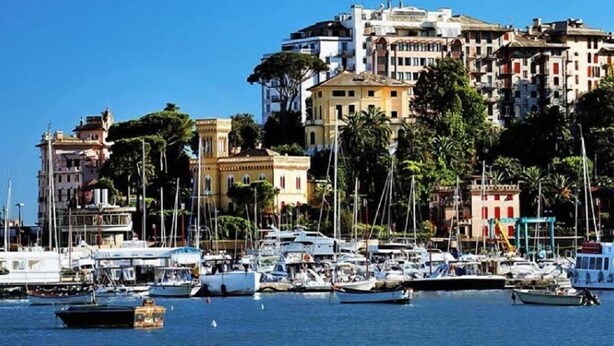 A marina with various boats docked, surrounded by buildings with balconies and palm trees. - Villa Cristina (Rapallo)