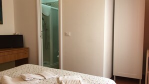 A hotel room with a bed, a wooden dresser, a television, a shower area, and a white wardrobe. - Villa Cristina (Rapallo)
