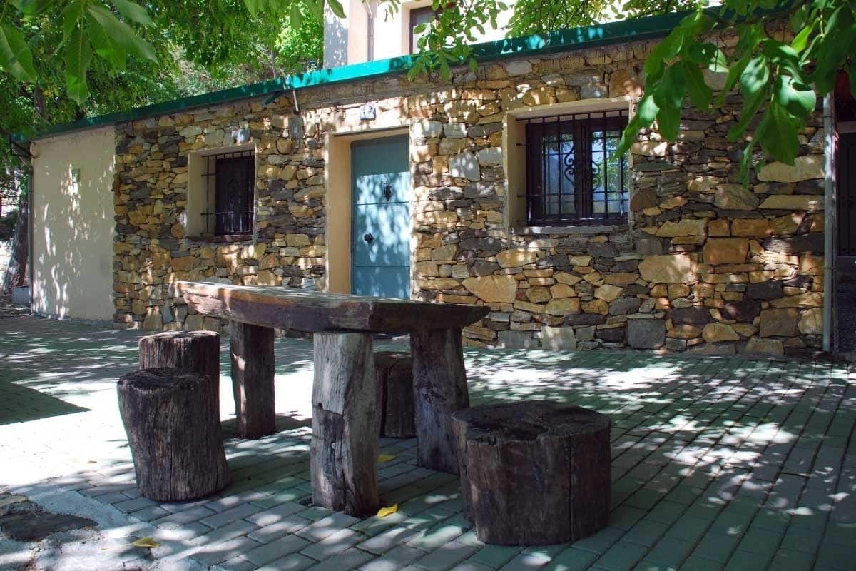Un bâtiment en pierre avec un toit végétalisé, un banc en bois et une porte.