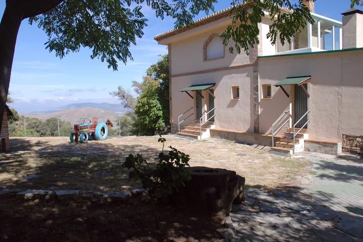 Un bâtiment à deux étages, doté d’un escalier en pierre menant à l’entrée, entouré d’un mur de pierre et agrémenté d’un petit jardin.