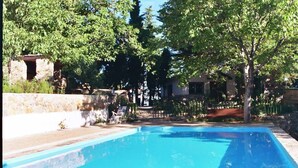 A rectangular swimming pool with clear blue water, surrounded by stone walls and lush greenery. - Casas Rurales Telecabina Las Catifas (Guejar Sierra)
