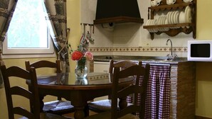 A kitchen with a round table, chairs, a vase with flowers, and a checkered cloth hanging over the counter. - Casas Rurales Telecabina Las Catifas (Guejar Sierra)