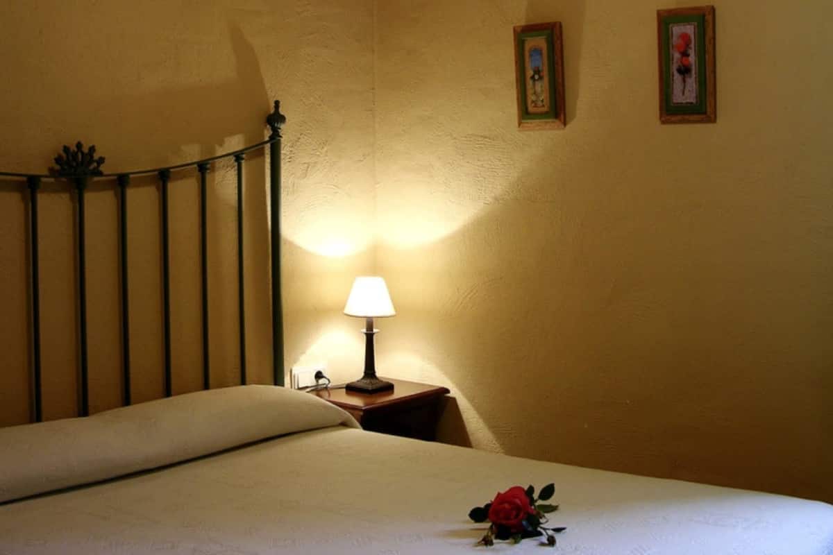 Un lit bien fait, agrémenté d’une seule rose rouge, d’une lampe de chevet et de deux tableaux encadrés accrochés au mur.
