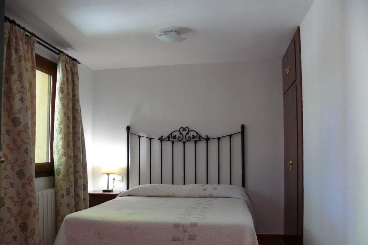 Une chambre avec un lit simple, une table de chevet, une fenêtre avec des rideaux et une armoire.