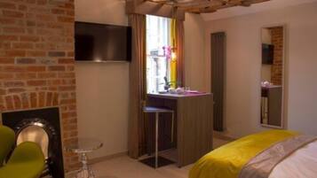 Une chambre d’hôtel avec un mur en briques, un téléviseur à écran plat fixé au-dessus d’une cheminée, un bureau avec une chaise, un lit recouvert d’une courtepointe jaune et une fenêtre avec des rideaux.