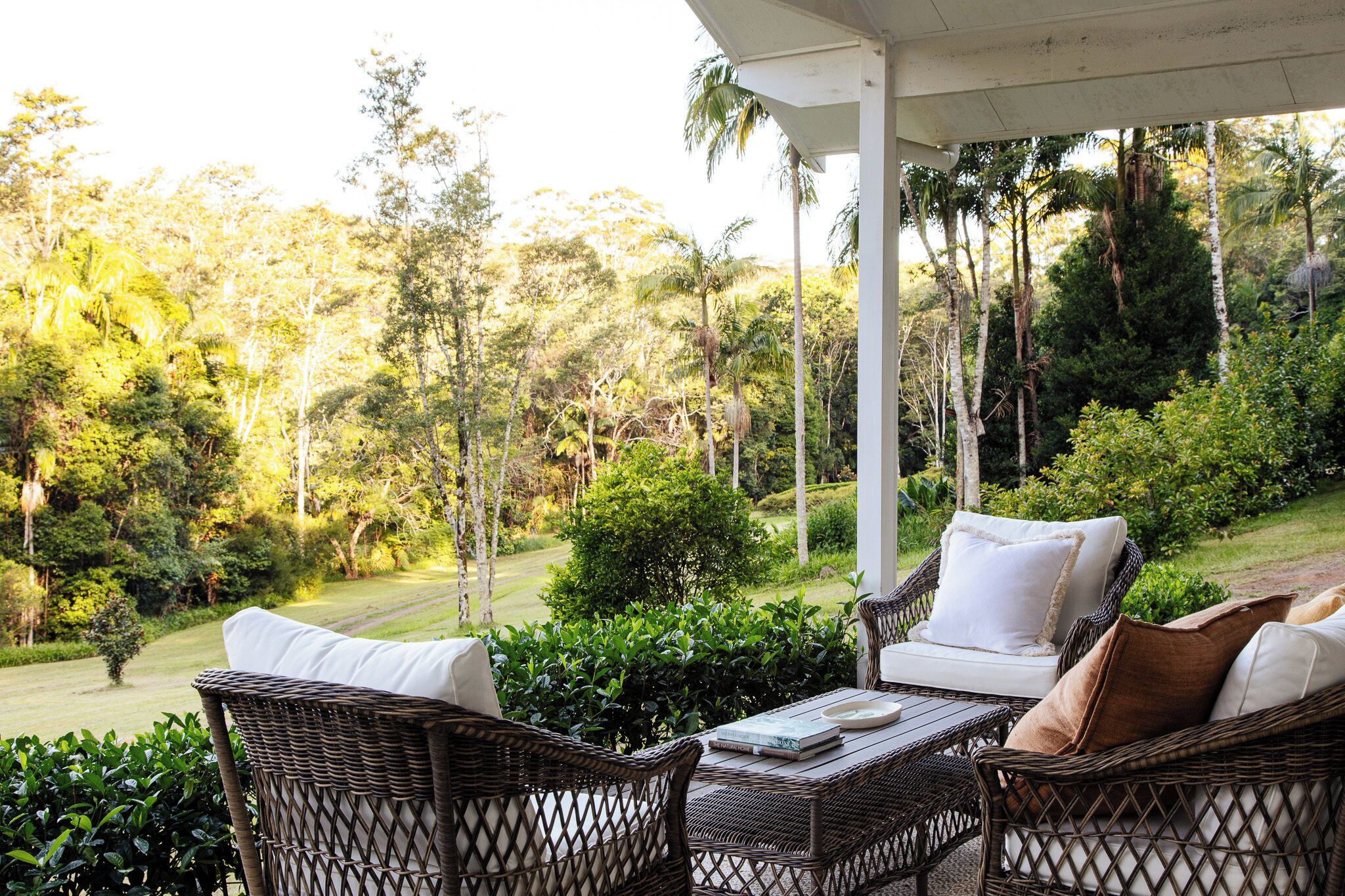 Un espace extérieur aménagé, abrité et doté de mobilier en osier, offrant une vue sur un jardin luxuriant et des arbres.