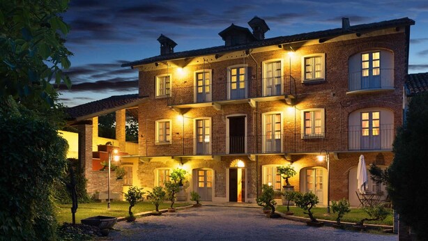 A multi-story brick building with a courtyard, featuring a central entrance, multiple windows, and outdoor lighting. - Risveglio in Langa (La Morra)