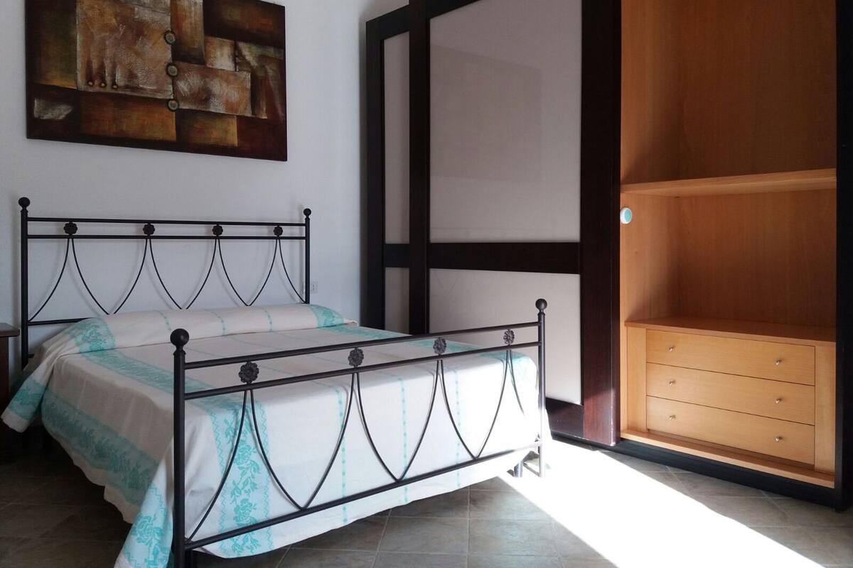 A bedroom with a bed, a wooden wardrobe, and a painting on the wall.