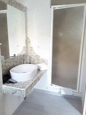 Un baño con lavamanos de diseño de piedra, un espejo y cabina de ducha.
