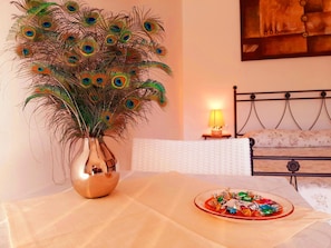 Una habitación con una cama, una mesita de noche con una lámpara, y una mesa con un plato de caramelos de colores.