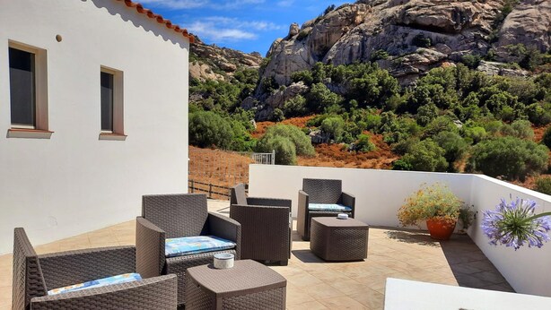 A rooftop patio with wicker furniture, a potted plant, and a view of rocky hills. - Lu Lisandru (Arzachena)