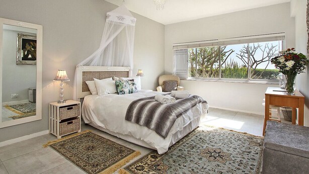 Une chambre à coucher avec un lit à baldaquin, une grande fenêtre donnant sur un beau paysage, une table de chevet avec une lampe et un miroir au mur.