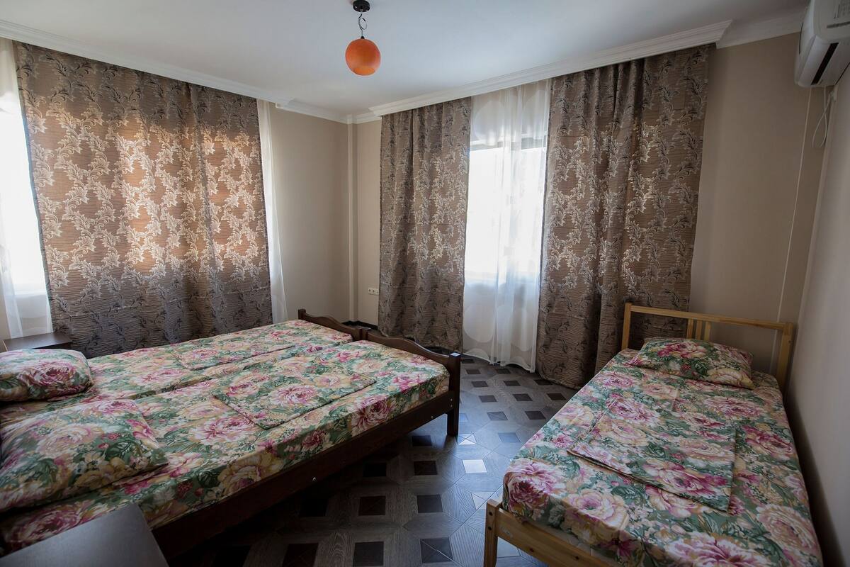 A room with two wooden beds, floral bedding, patterned curtains, and a tiled floor.