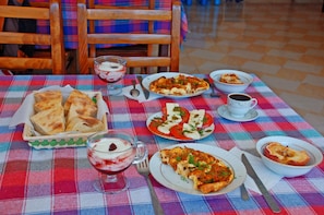 Ein Tisch mit verschiedenen Gerichten, darunter Pizza, Joghurt und eine Tasse Kaffee.