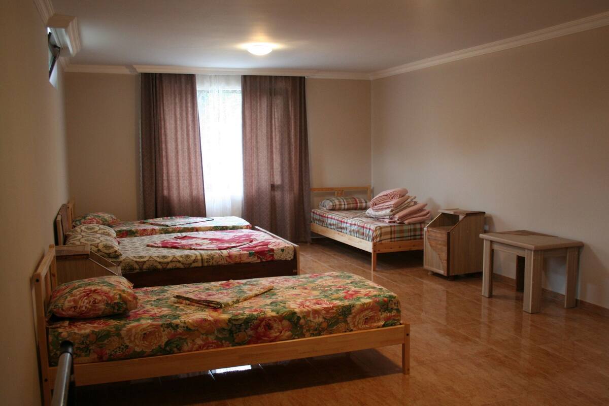 A room with two wooden beds, a wooden nightstand, a small wooden table, and a window with curtains.