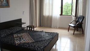 Un dormitorio con cama, una silla, un cuadro y una ventana con cortinas.