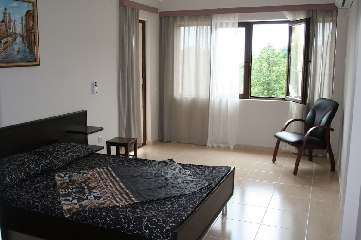 A bedroom with a bed, a chair, a painting, and a window with curtains.
