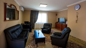 Una sala de estar con un sofá, dos sillones, una mesa de centro, un televisor y un reloj en la pared.