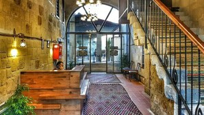 Un hall d’hôtel avec un comptoir d’accueil en bois, un escalier et un lustre.