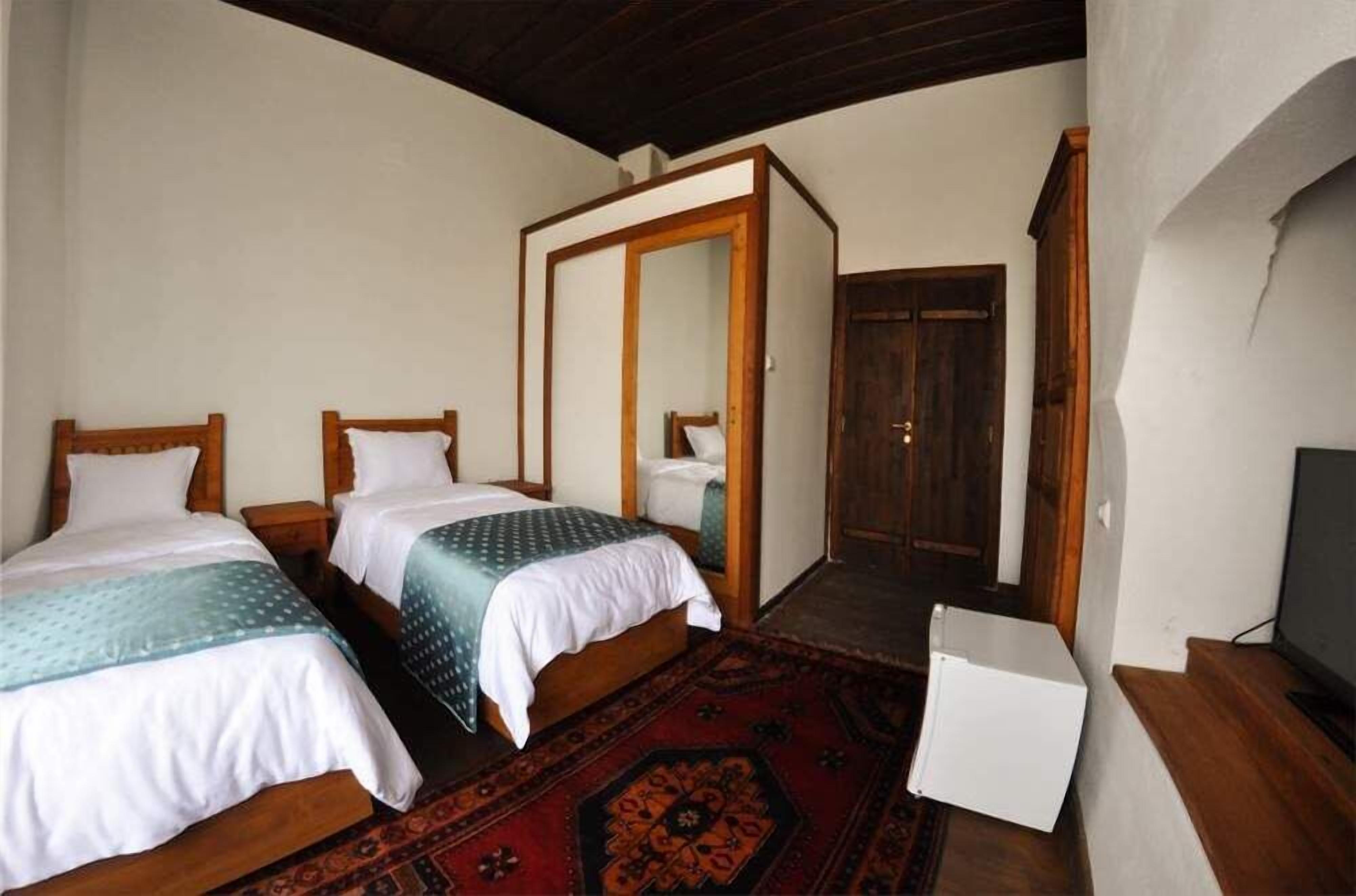 A bedroom with two beds, a wardrobe, a television, and a small white cabinet.
