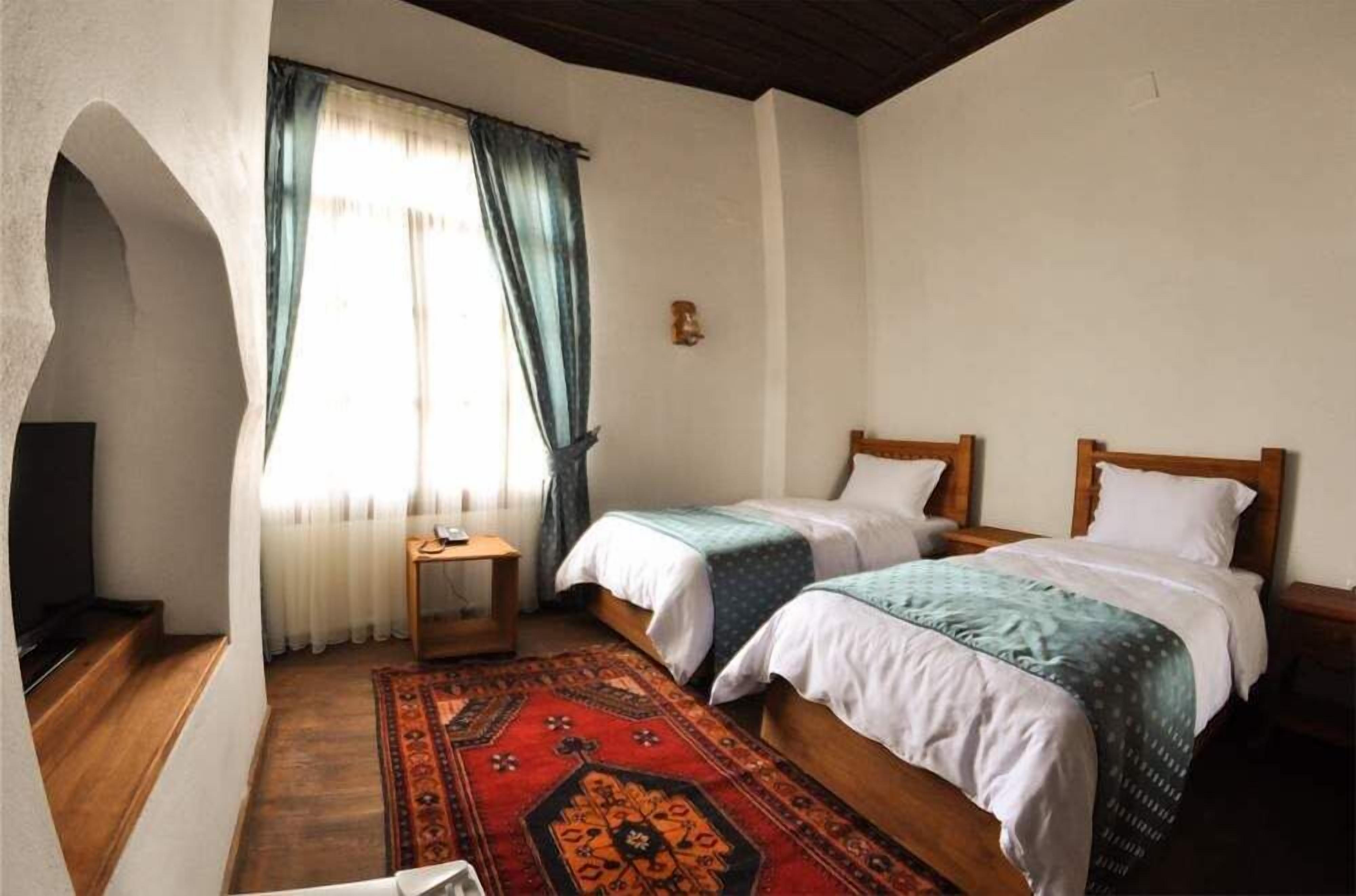 Een kamer met twee bedden, een klein tafeltje, een televisie en een raam met gordijnen.