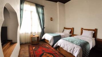 Een kamer met twee bedden, een klein tafeltje, een televisie en een raam met gordijnen.