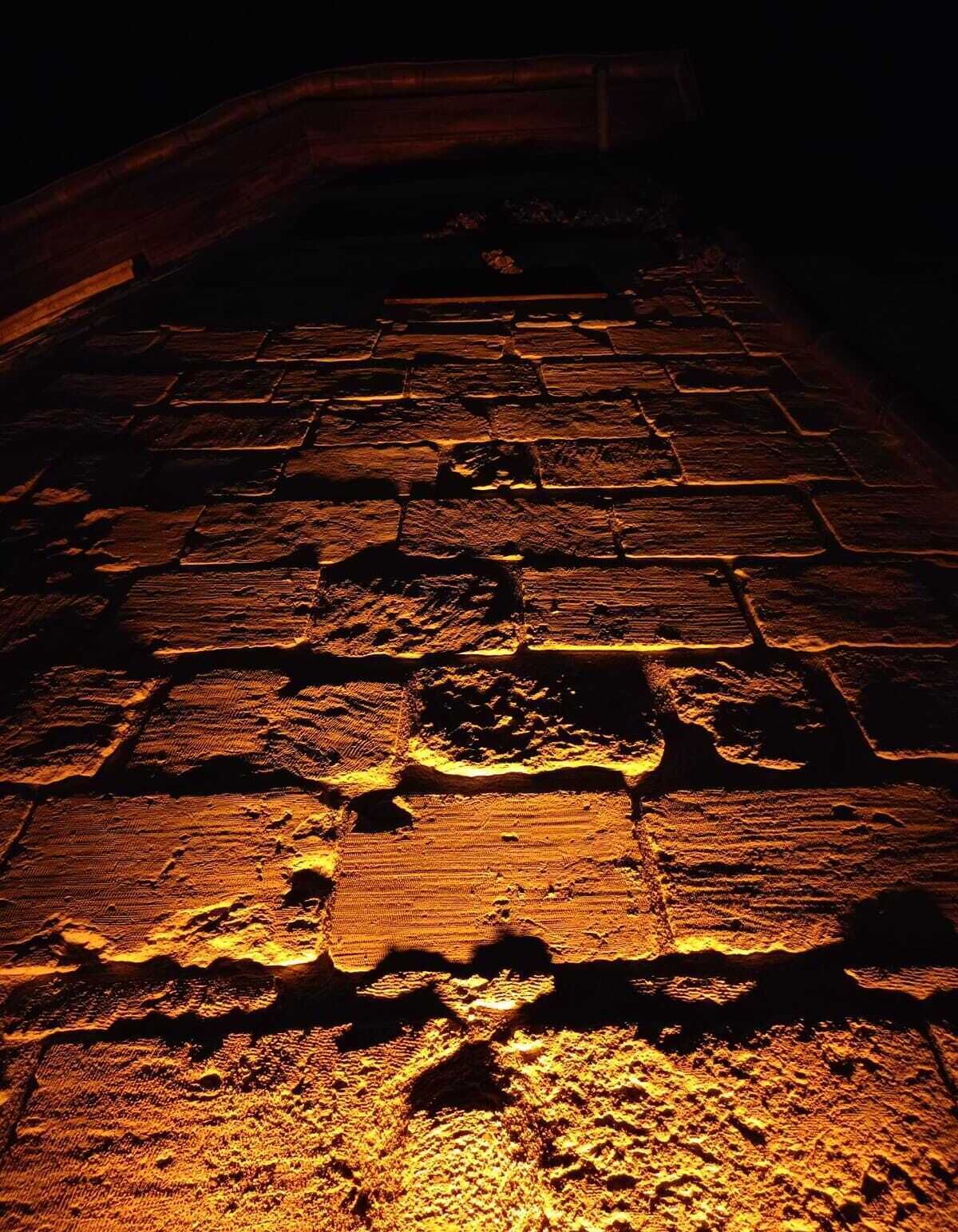 A stone pathway illuminated by warm lighting, leading to a dark doorway.