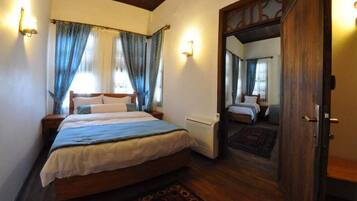 A bedroom with a wooden bed, two bedside tables, a nightstand, a mirror, and a door.