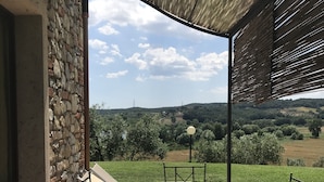 Un patio al aire libre con un muro de piedra, una mesa con sillas y vistas a un paisaje verde.