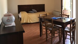 Una habitación con cama, una mesa con sillas, un hervidor y una lámpara colgante.