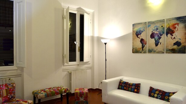 A living room with a white sofa, colorful cushions, a glass coffee table, a bench with a floral cushion, a standing lamp, and a world map artwork on the wall. - Ariete (Florence)