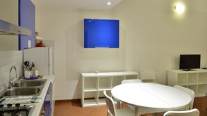 A modern kitchen with a sink, stove, and a blue cabinet. There is a white dining table with chairs and a TV on a stand. - Ariete (Florence)