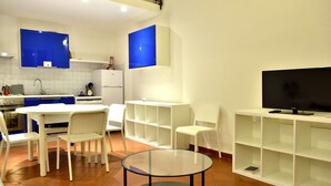 A modern kitchen with white cabinets, a white dining table, and chairs. There is a TV on a stand and a bookshelf. - Ariete (Florence)