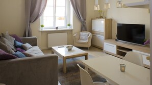 A living room with a sofa, a coffee table, a TV, and a dining area with a table and chairs. - Rais Serviced Apartments (Warsaw)