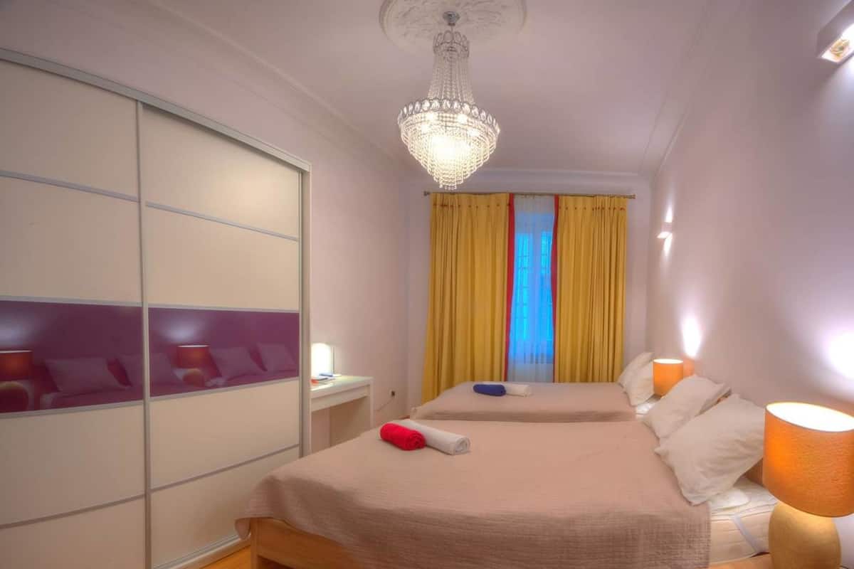 A hotel room with two beds, a large mirror, a chandelier, and yellow curtains.