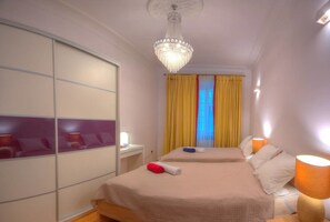 A hotel room with two beds, a large mirror, a chandelier, and yellow curtains.