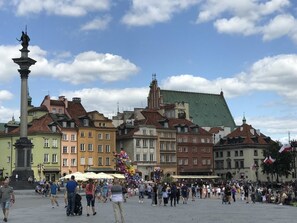A public square with historic buildings, a central monument, and a crowd of people.