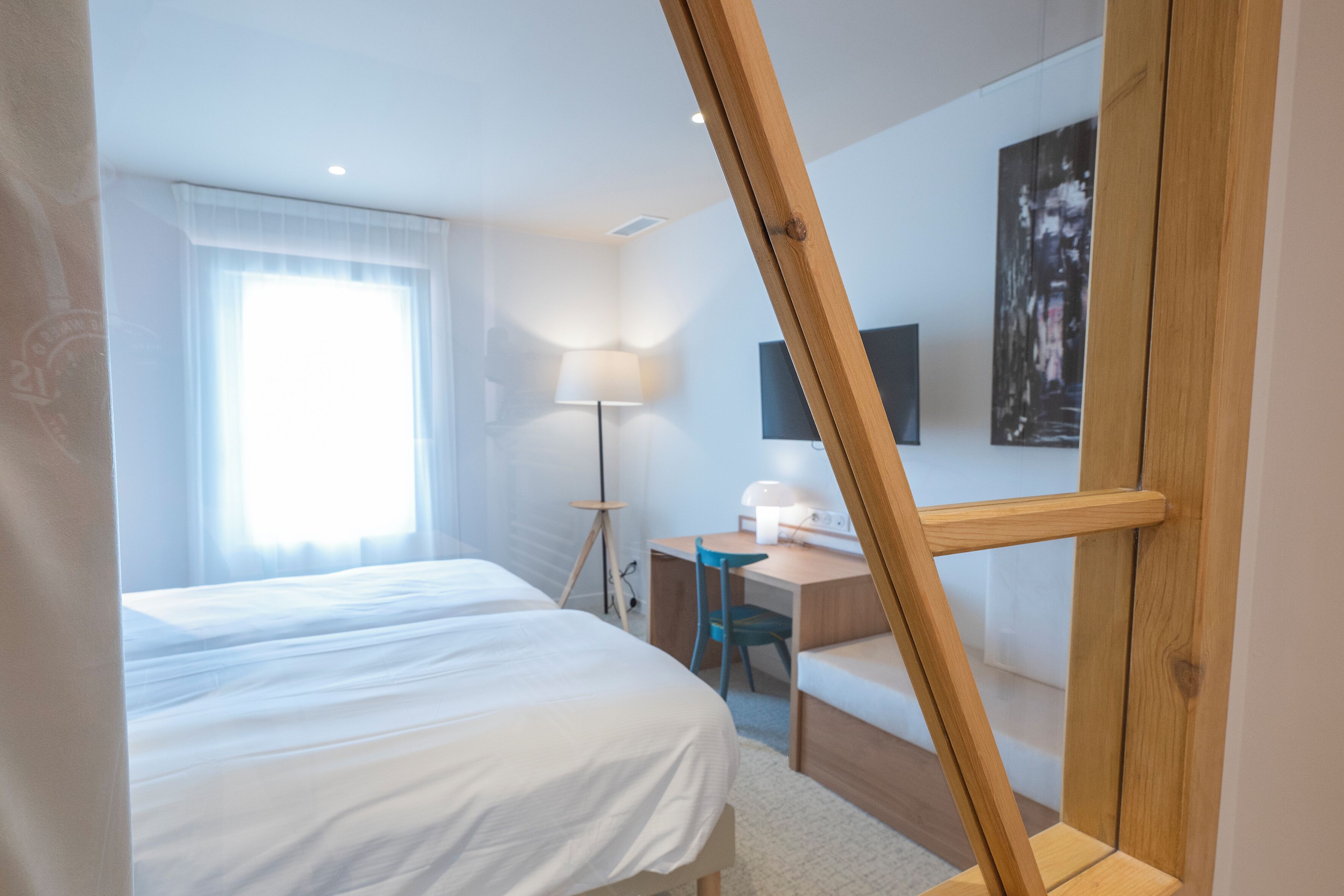 A hotel room with a bed, desk, chair, lamp, and artwork on the wall.