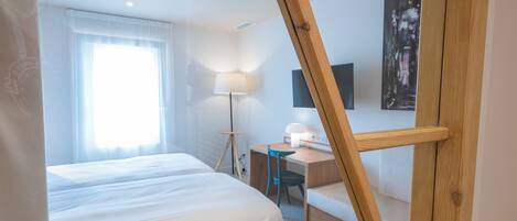 A hotel room with a bed, desk, chair, lamp, and artwork on the wall.