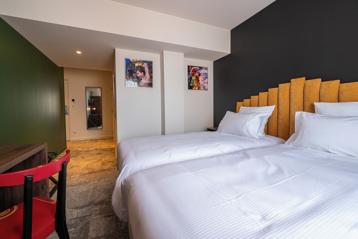 A hotel room with two beds, a wooden headboard, and artwork on the walls.