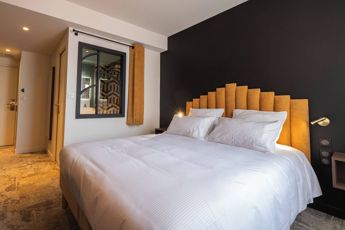 Una habitación de hotel moderna con una cama grande, una pared de acento oscura y un cabecero de madera.