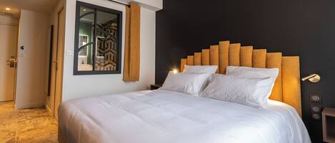 A modern hotel room with a large bed, a dark accent wall, and a wooden headboard.