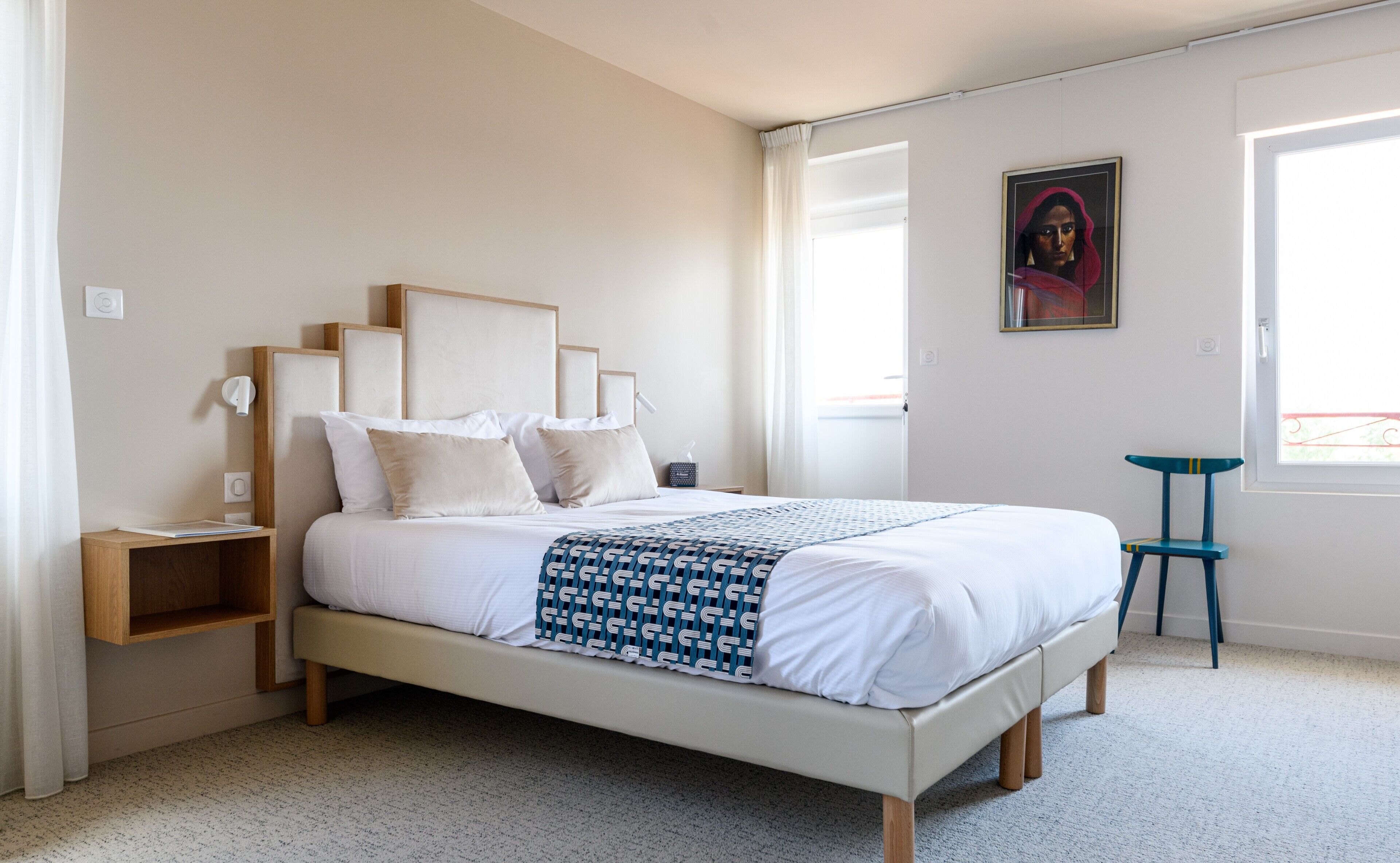 A neatly arranged bedroom with a bed, bedside tables, a chair, and a painting on the wall.