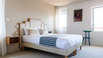 A neatly arranged bedroom with a bed, bedside tables, a chair, and a painting on the wall.