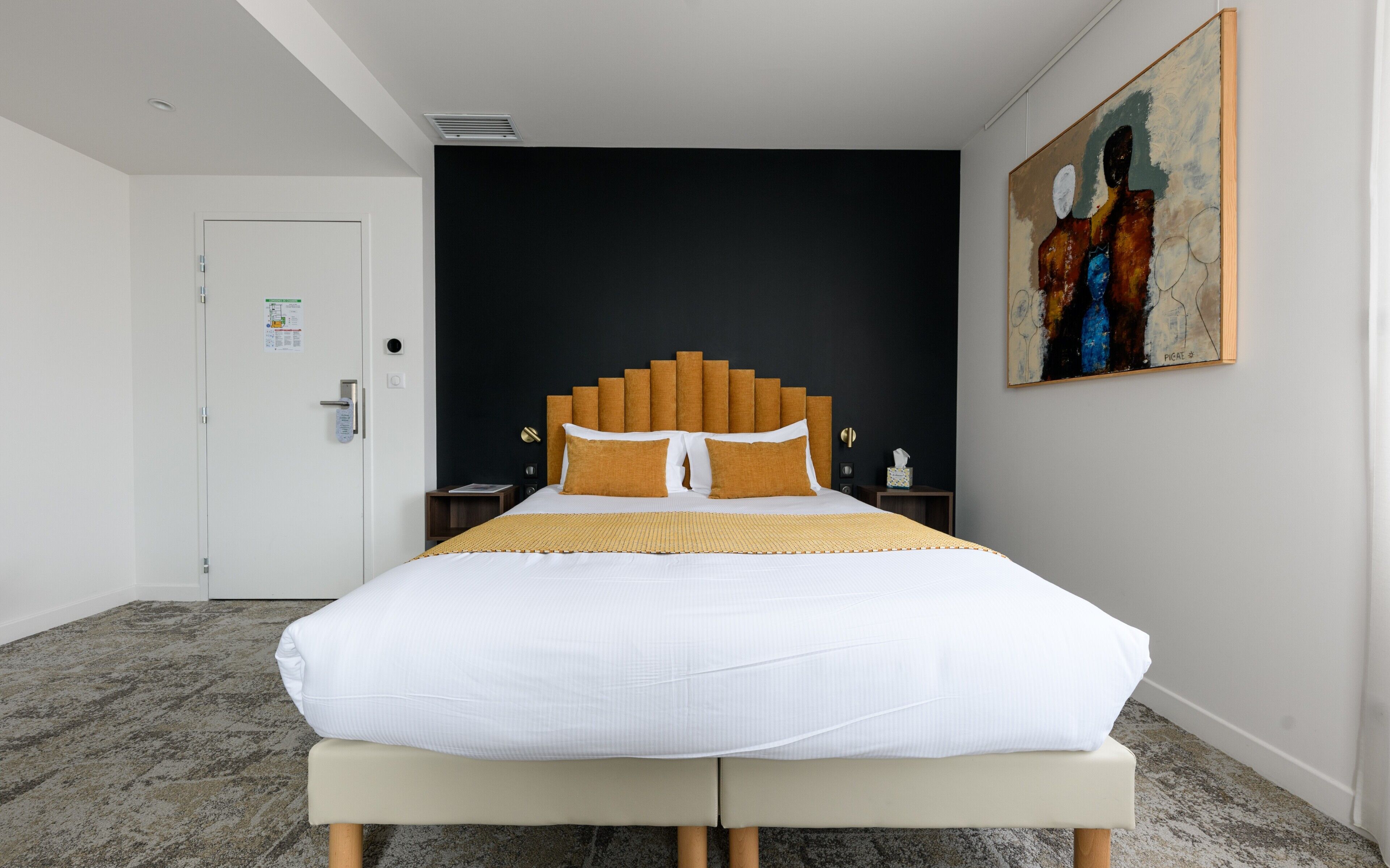 A modern hotel room with a large bed, a dark accent wall, and a painting on the wall.