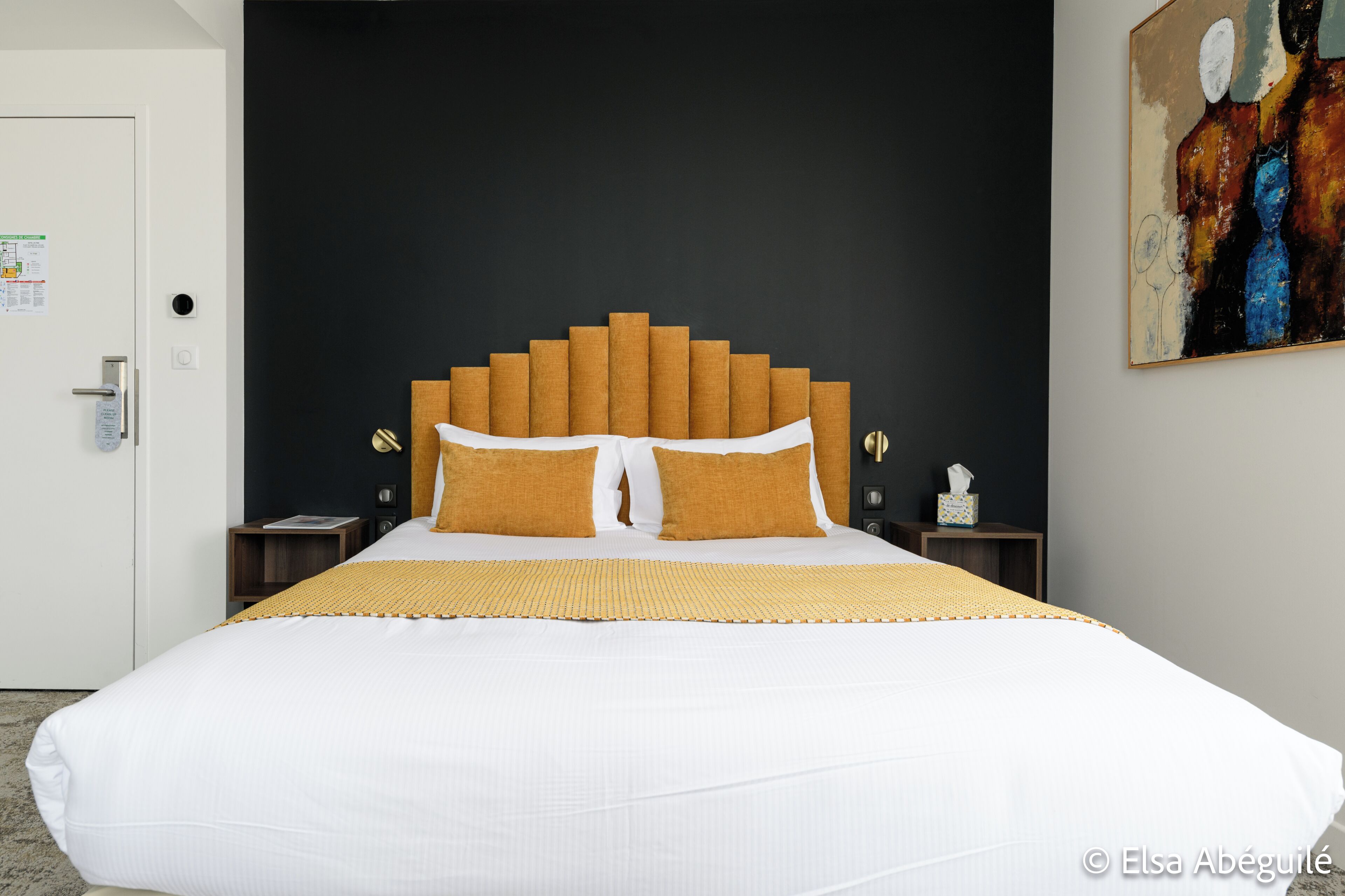 Una habitación de hotel con una cama grande, una pared oscura y un cuadro.