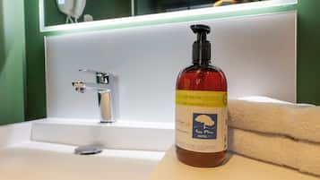 Ein Badezimmer mit einem weißen Waschbecken, einem Spiegel und einer Duschgel-Flasche auf dem Waschbecken.
